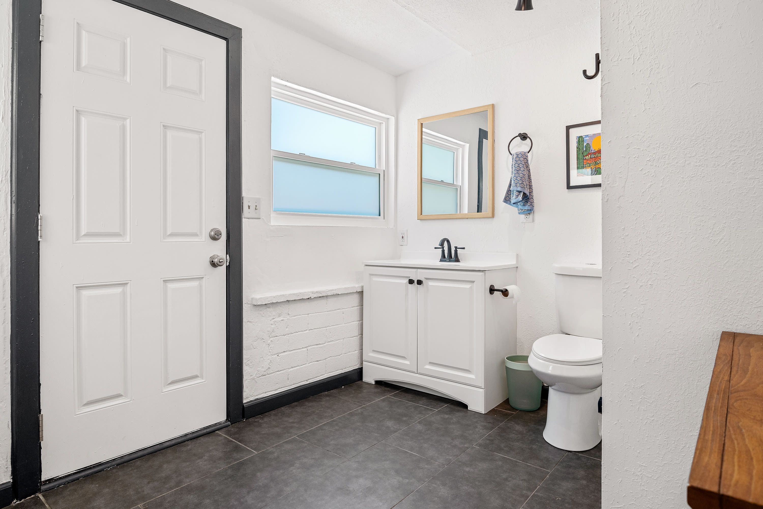A bathroom with a white door, a window, a sink, a mirror, and a toilet.