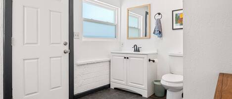 A bathroom with a white door, a window, a sink, a mirror, and a toilet.