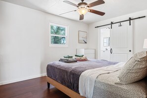 Un dormitorio con cama, ventilador de techo, ventana y puerta.