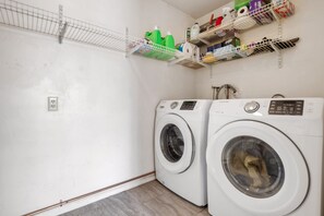 A laundry room with two front-loading washing machines and shelves above containing cleaning supplies. - Sonoran Velo (Tucson)