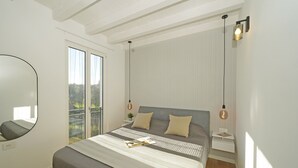 A modern bedroom with a large bed, a bedside table, a nightstand, a mirror, and a balcony with a view.