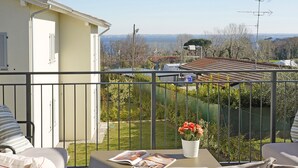 A balcony with a table, a potted plant, and a view of a garden and buildings.