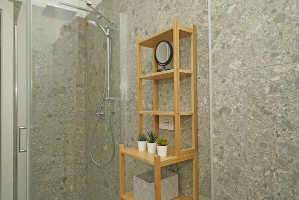 A bathroom with a shower, a wooden shelf with a mirror, and two potted plants.