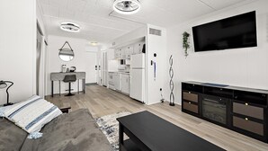 A modern living room with a sofa, a coffee table, a TV, and a kitchen area with white appliances. - Direct Oceanfront with Pool - Steps To The Beach (Ocean City)