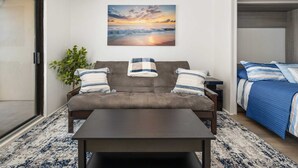 A modern living room with a sofa, a coffee table, and a painting of a sunset over the ocean. - Direct Oceanfront with Pool - Steps To The Beach (Ocean City)