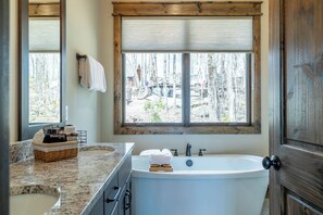 A bathroom with a large window, a bathtub, a sink, and a wooden door. - Grayling Lodge at Eagles Nest (Banner Elk)