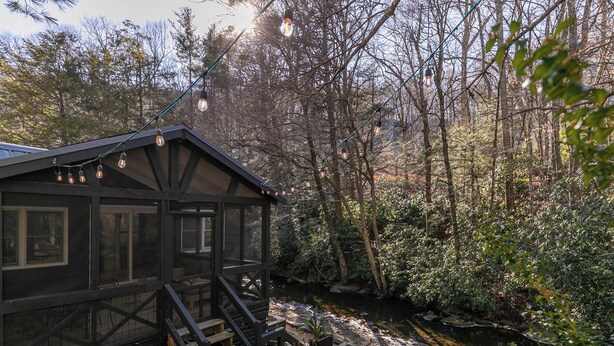 A cabin with a wooden exterior, a staircase leading to a deck, and a pond in the background. - Anglers Cottage (Blowing Rock)