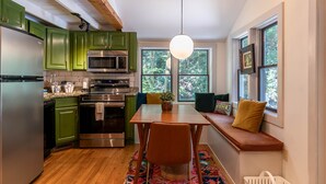 A kitchen with green cabinets, stainless steel appliances, a wooden dining table, and a window seat with cushions. - Anglers Cottage (Blowing Rock)