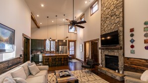 A spacious living room with a fireplace, a kitchen area, and a bar. - Doe Run Cottage at Eagles Nest (Banner Elk)
