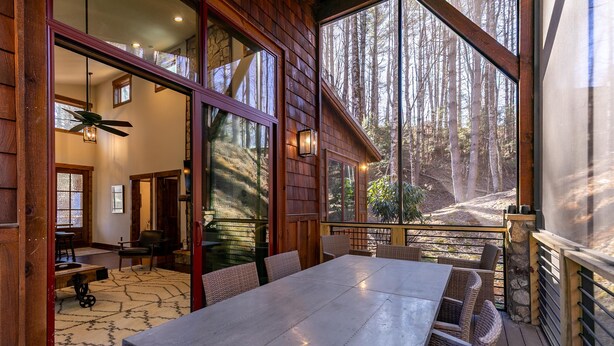 A wooden deck with a dining table and chairs, a ceiling fan, and a view of a forested area. - Doe Run Cottage at Eagles Nest (Banner Elk)