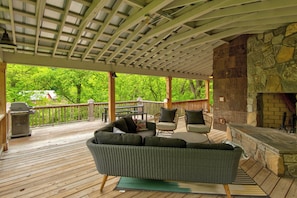 A covered outdoor deck with a stone fireplace, wicker furniture, and a grill. - Orchard House (Banner Elk)
