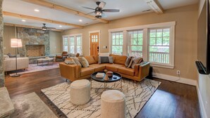 A spacious living room with a large sectional sofa, a fireplace, stone walls, and large windows offering a view of the outdoors. - Orchard House (Banner Elk)
