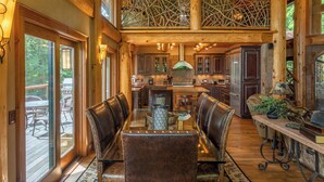 A spacious dining area with a high ceiling and exposed wooden beams, a central island with a sink, and leather-upholstered chairs. - Big Bear Lodge at Eagles Nest (Banner Elk)