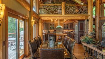 A spacious dining area with a high ceiling and exposed wooden beams, a central island with a sink, and leather-upholstered chairs.