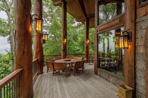 Una terraza de madera con una mesa redonda y sillas, rodeada de barandas de madera y grandes ventanales que ofrecen vistas al bosque.