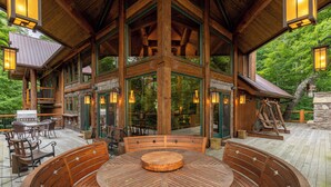 A wooden deck with a round table and benches, surrounded by glass doors and windows, overlooking a forested area. - Big Bear Lodge at Eagles Nest (Banner Elk)