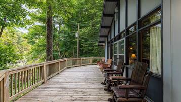 A wooden deck with chairs and a table, surrounded by trees.