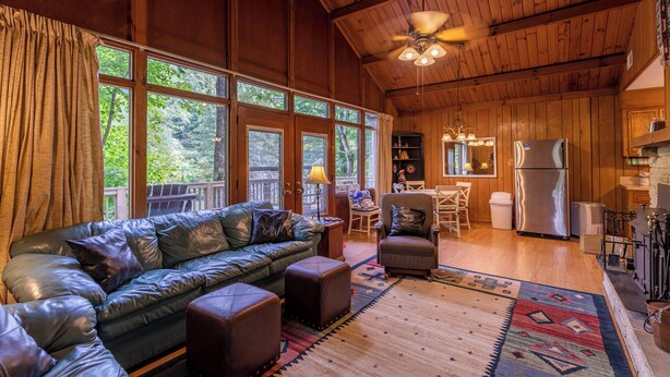 A cozy cabin interior with a leather sofa, ottomans, a dining area, and a kitchen. - Rivers Edge in Todd (Todd)