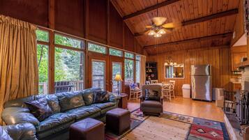 A cozy cabin interior with a leather sofa, ottomans, a dining area, and a kitchen.
