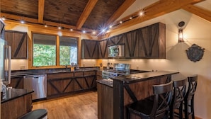A rustic kitchen with wooden cabinets, a stainless steel refrigerator, a built-in stove, and a bar area with stools. - Rustic Cedar Rock Townhome at Eagles (Banner Elk)