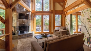 A cozy living room with a stone fireplace, wooden beams, large windows, and a sofa. - Modern Cedar Rock Townhome at Eagles (Banner Elk)