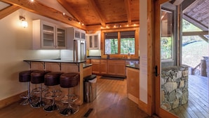 A kitchen with wooden beams, a bar area with stools, and a stone accent wall. - Modern Cedar Rock Townhome at Eagles (Banner Elk)