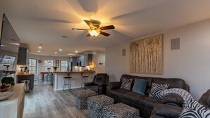 Ein geräumiges Wohnzimmer mit einer dunkelbraunen Ledersofa, Zebra-Muster-Pouffen und einem Deckenventilator.