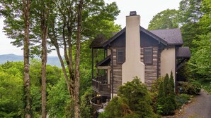 A two-story log cabin with a balcony, surrounded by dense forest and a view of the mountains. - Mount Ever-Rest (Banner Elk)