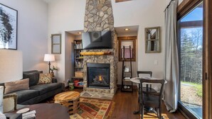 A cozy living room with a stone fireplace, a comfortable sofa, a coffee table, and a dining area with a table and chairs. - Hilltop Hideout at Eagles Nest (Banner Elk)