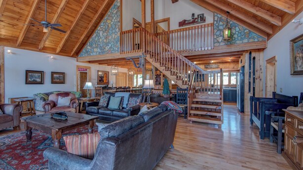 A spacious living area with a high ceiling, wooden beams, a staircase, and a view of the kitchen. - Boles Lodge (Boone)