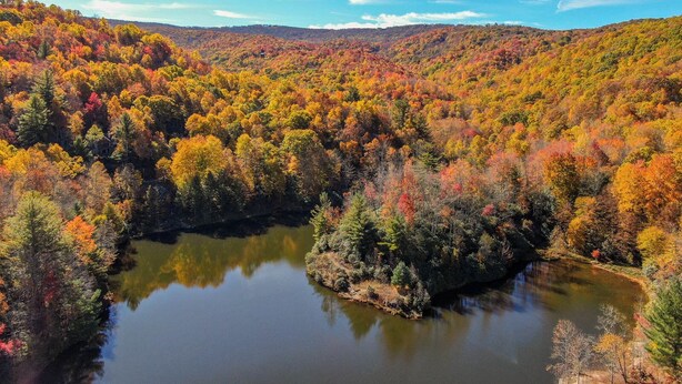 A serene landscape with a lake surrounded by autumn-colored trees and a distant mountain range. - Lake Overlook (Banner Elk)