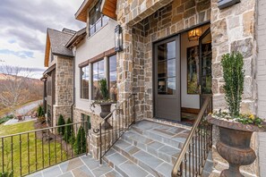 Une maison en pierre avec un escalier en pierre menant à la porte d’entrée, un petit espace extérieur aménagé avec des chaises, et une vue sur une rivière.