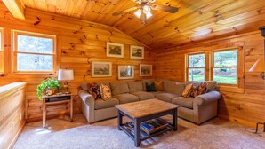 A cozy log cabin interior with a sectional sofa, a coffee table, and framed artwork on the walls. - Hemlock Hideaway (Boone)
