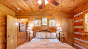 A wooden-paneled bedroom with a bed, framed botanical prints on the wall, and a ceiling fan. - Hemlock Hideaway (Boone)