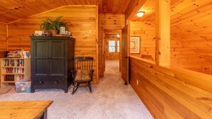 A wooden cabin interior with a bookshelf, a cabinet, and a chair. - Hemlock Hideaway (Boone)