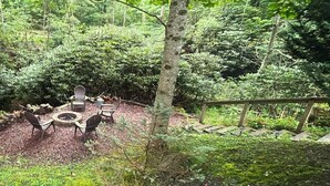 A forested outdoor area with a fire pit and seating. - Hemlock Hideaway (Boone)