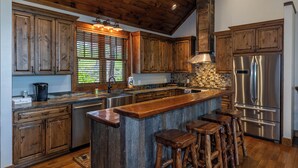 Una cocina con armarios de madera, un refrigerador de acero inoxidable y una barra con taburetes.