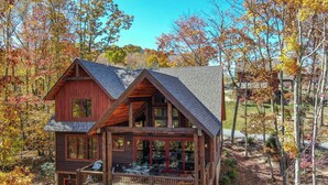 Une cabane en bois à deux étages, dotée d’un balcon et entourée du feuillage automnal.