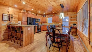 A wooden cabin interior with a kitchen, dining area, and a large window. - 1 Abundant Life (Vilas)