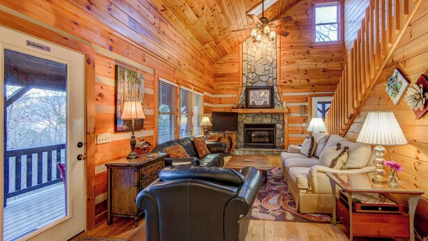 A cozy cabin interior with a stone fireplace, wooden walls, a black leather sofa, and a wooden staircase. - 1 Abundant Life (Vilas)