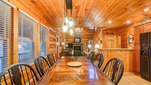 A wooden interior with a long dining table, chairs, and a kitchen area with a refrigerator. - 1 Abundant Life (Vilas)