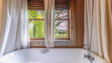 A bathroom with a bathtub, wooden window frames, and white curtains.