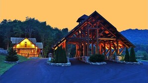 A wooden cabin with a porch and a separate building with a sloped roof, surrounded by trees and a mountain in the background. - Antler Ridge at Eagles Nest (Elk Park)