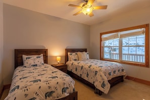 A bedroom with two beds, a ceiling fan, a nightstand with a lamp, and a window with a view of snow outside. - Lazy Bear Inn (Sugar Grove)