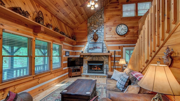 A cozy cabin interior with a stone fireplace, wooden walls, and a large window overlooking a forest. - Crosswind (Vilas)