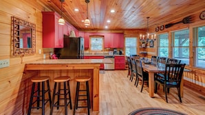 A wooden cabin interior with a kitchen, dining area, and bar stools. - Crosswind (Vilas)