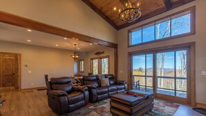 A spacious living room with leather sofas, a large window, and a high ceiling with exposed beams. - Hidden Gem at Eagles Nest (Banner Elk)
