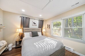Un dormitorio con cama, lámparas de noche, una mesita de noche, una ventana con persianas y un cuadro colgado en la pared.