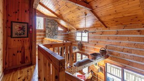A wooden cabin interior with a loft bedroom, stone wall, wooden beams, and a fireplace. - Daniel Boone Lodge (Boone)