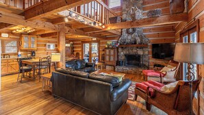 A spacious log cabin interior with a stone fireplace, leather sofa, and wicker furniture. - Daniel Boone Lodge (Boone)